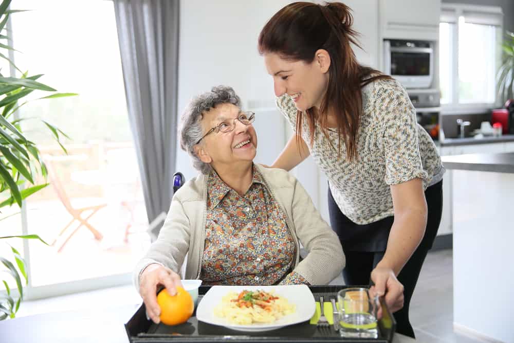 Caregiver serving tray of food to senior patient