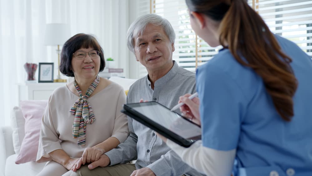 senior care caregiver in amicable conversation with elderly Asian couple