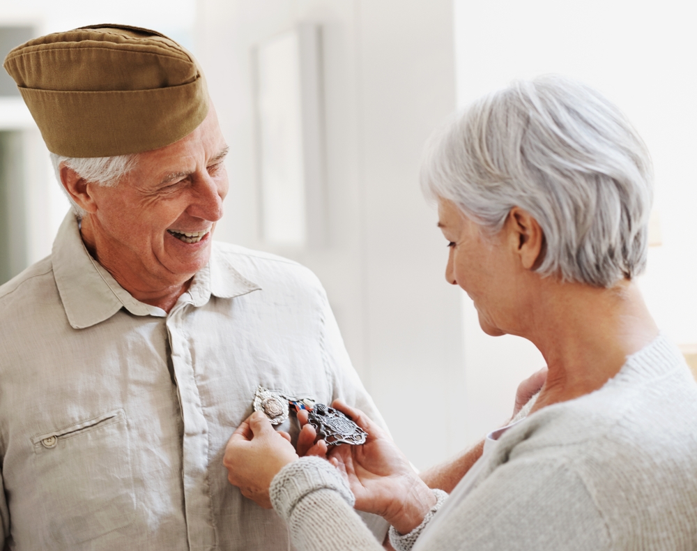 A female spouse of a male veteran examines the medals of honor which her spouse was decorated with. Smiles on their faces explain it all