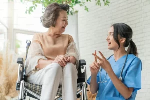 an elderly woman sitting in a wheelchair conversing with a younger female caregiver in a non-medical in-home care setting